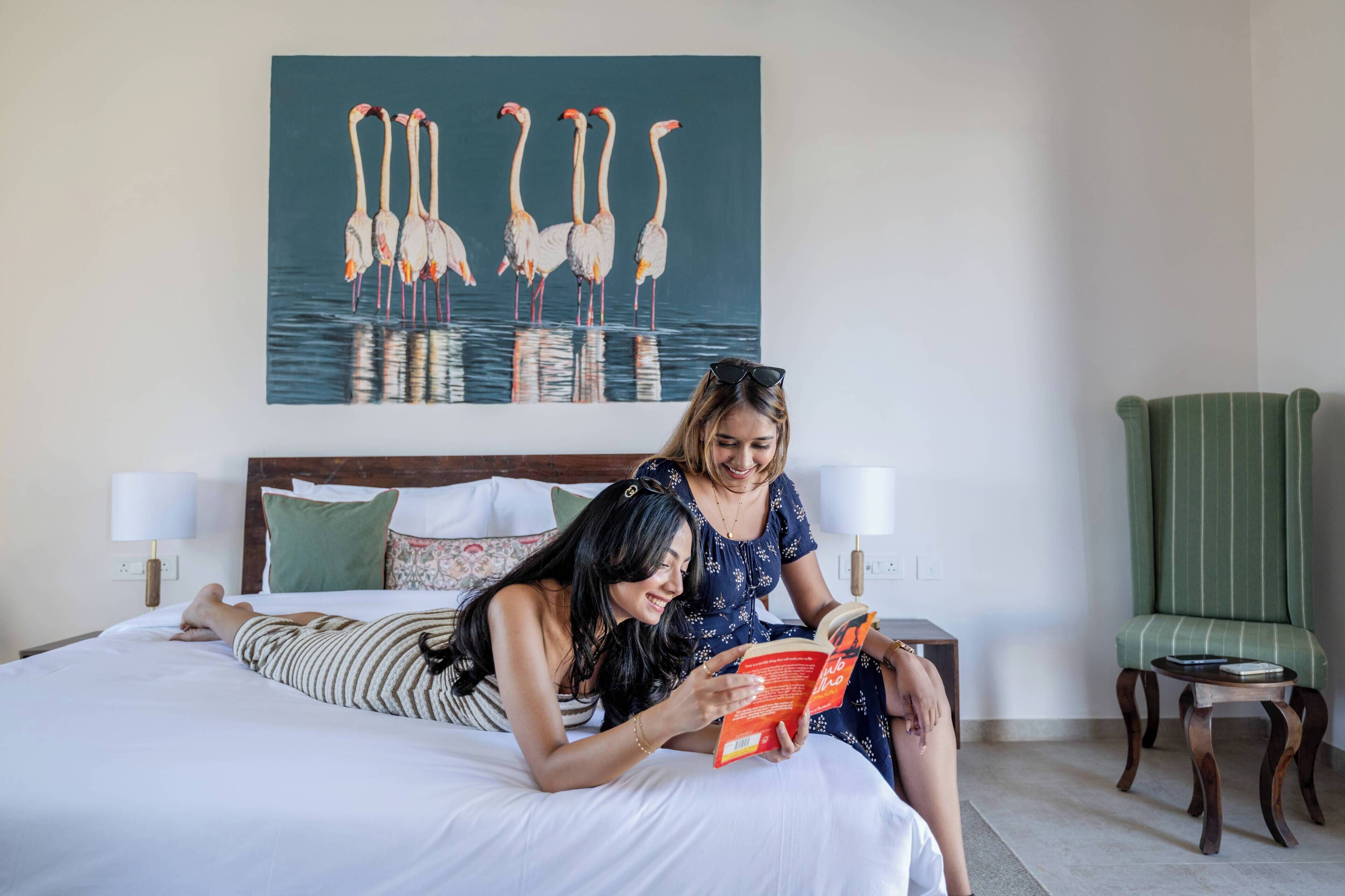 A hotel room with a bed, a reading lamp, a green striped chair, and a painting of flamingos on the wall.