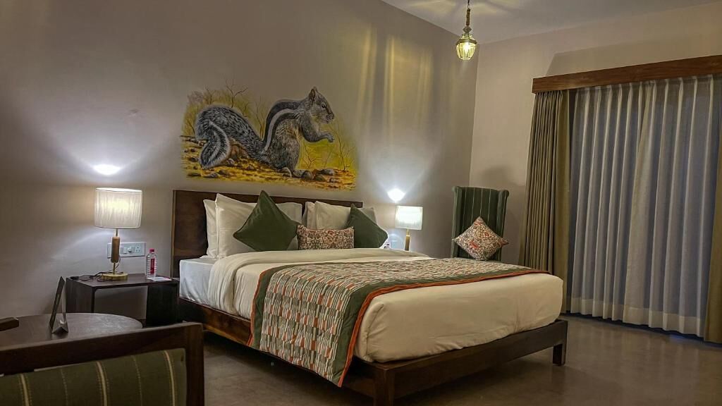 A hotel room with a bed, two bedside tables, a desk, a chair, a painting on the wall, and a window with curtains.