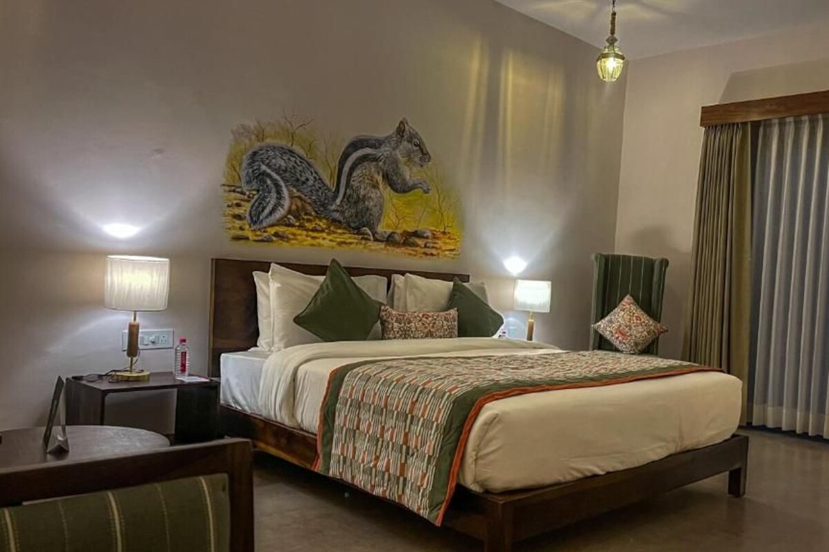 A hotel room with a bed, two bedside tables, a desk, a chair, a painting on the wall, and a window with curtains.