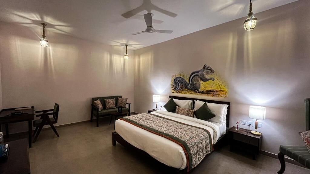A bedroom with a bed, a desk, a chair, a nightstand, and a wall-mounted artwork.