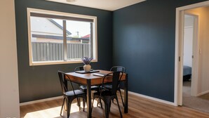 Un coin repas avec une table et des chaises en bois, une fenêtre donnant sur une clôture et une porte menant à une autre pièce.