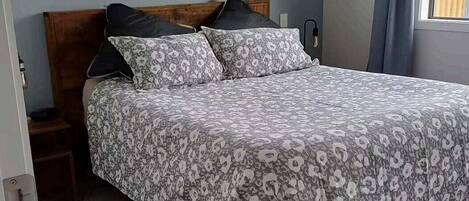 A bedroom with a bed, a nightstand, a window, and a curtain.