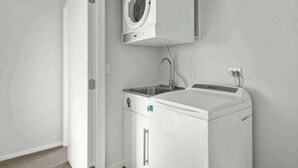 Une petite buanderie équipée d’un lave-linge, d’un évier et d’un meuble de rangement.