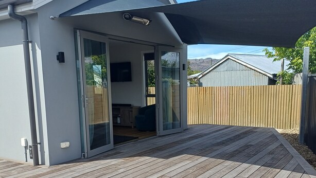 Une maison moderne dotée d’une terrasse en bois, de portes-fenêtres coulissantes et d’un téléviseur fixé au mur.