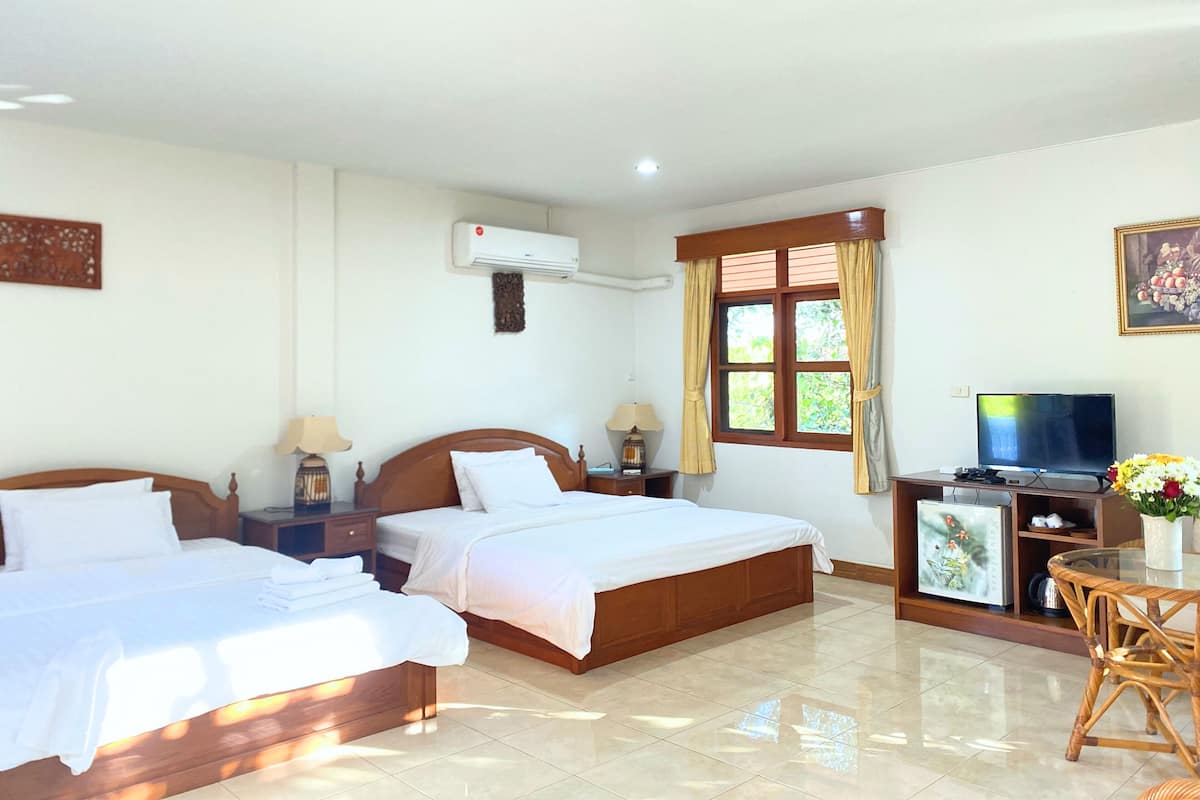 A hotel room with two beds, a TV, a desk with a computer, and a small table with flowers.