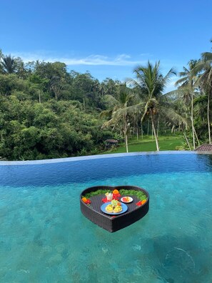 Piscina infinita com área de refeições flutuante, incluindo um prato de comida e uma bebida.