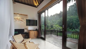 A room with a balcony, wicker chairs, a TV, and a kitchen area. - The Tirta Sari Villas (Tegallalang)