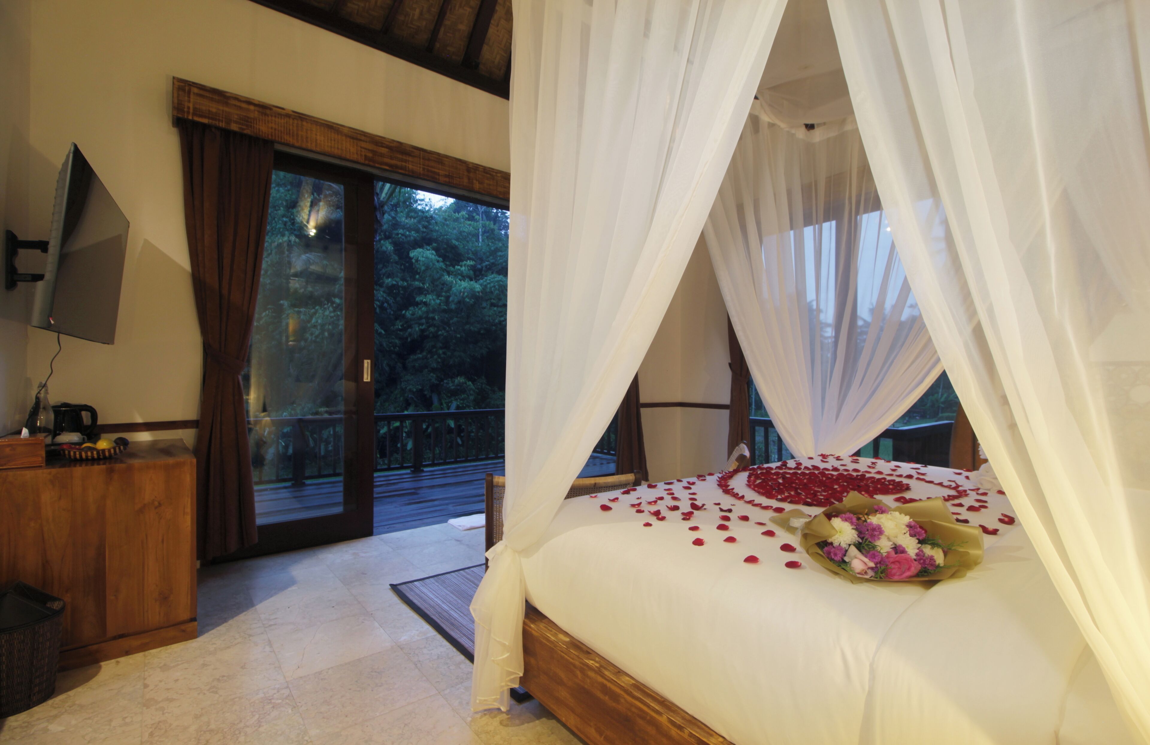 A bedroom with a bed, a wooden dresser, a television, and a balcony with glass doors.