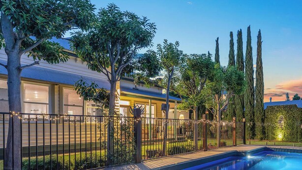 Una piscina con una terraza pavimentada, rodeada por una valla y árboles.