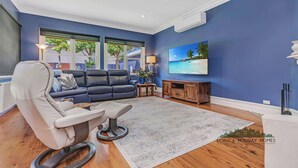 Una sala de estar moderna con una pared azul, un ventanal grande, un sofá, una silla, una mesita de centro, un televisor y un mueble de madera.