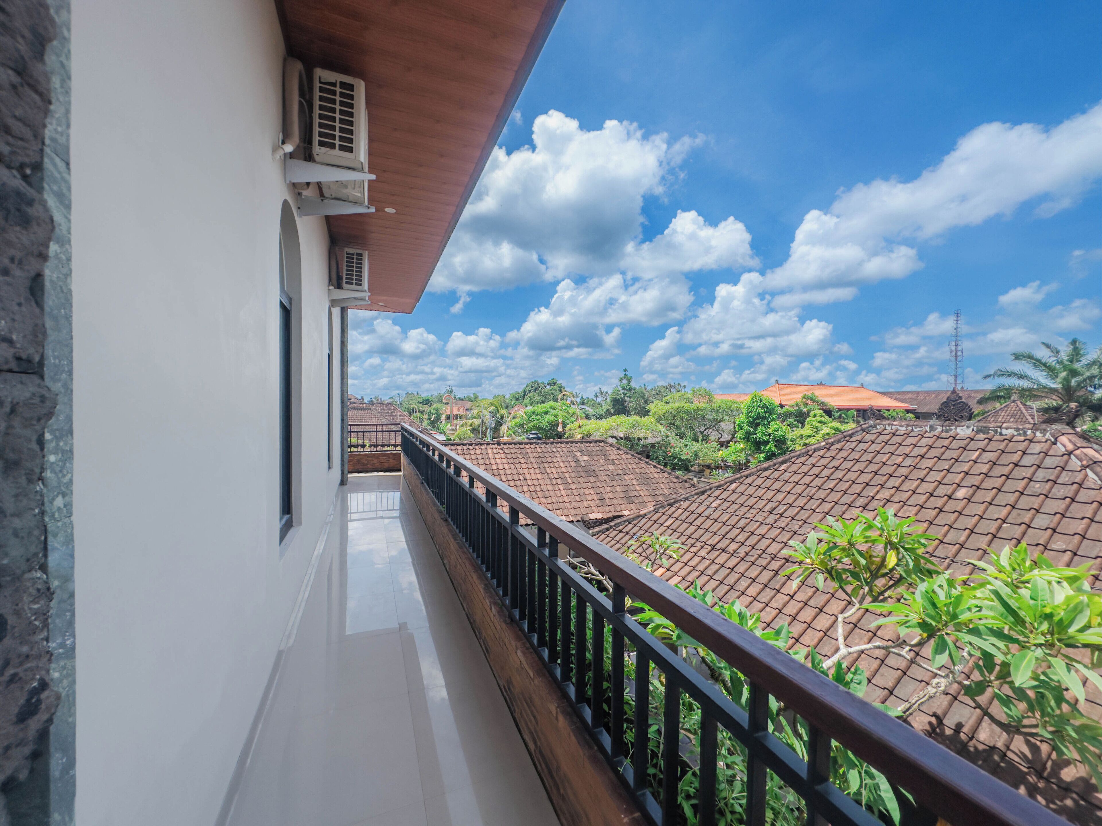 A balcony with a view of terracotta-roofed buildings and greenery under a partly cloudy sky.
