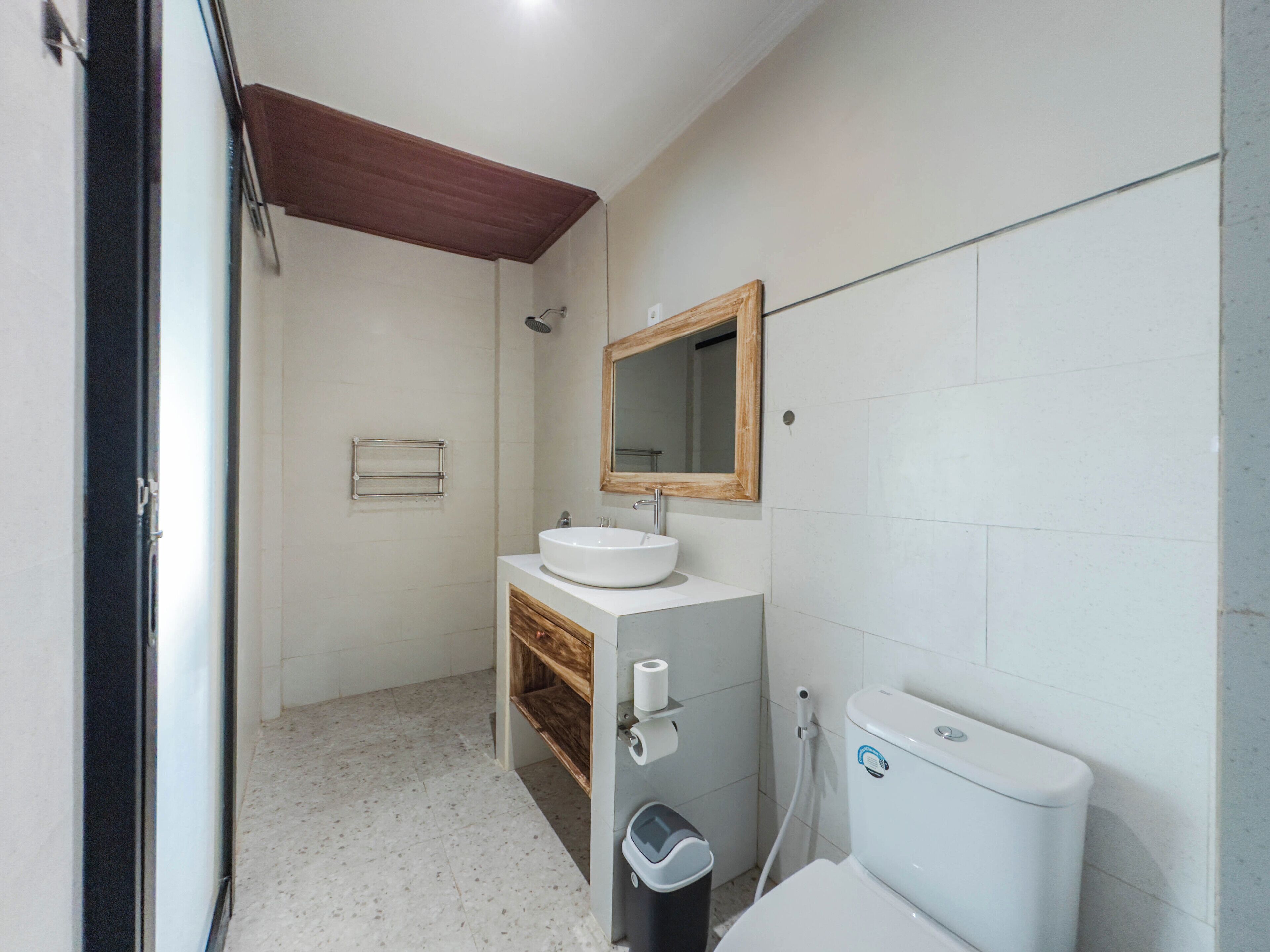 Une salle de bain avec un lavabo blanc, un meuble-lavabo en bois, un miroir, des toilettes et un espace douche.