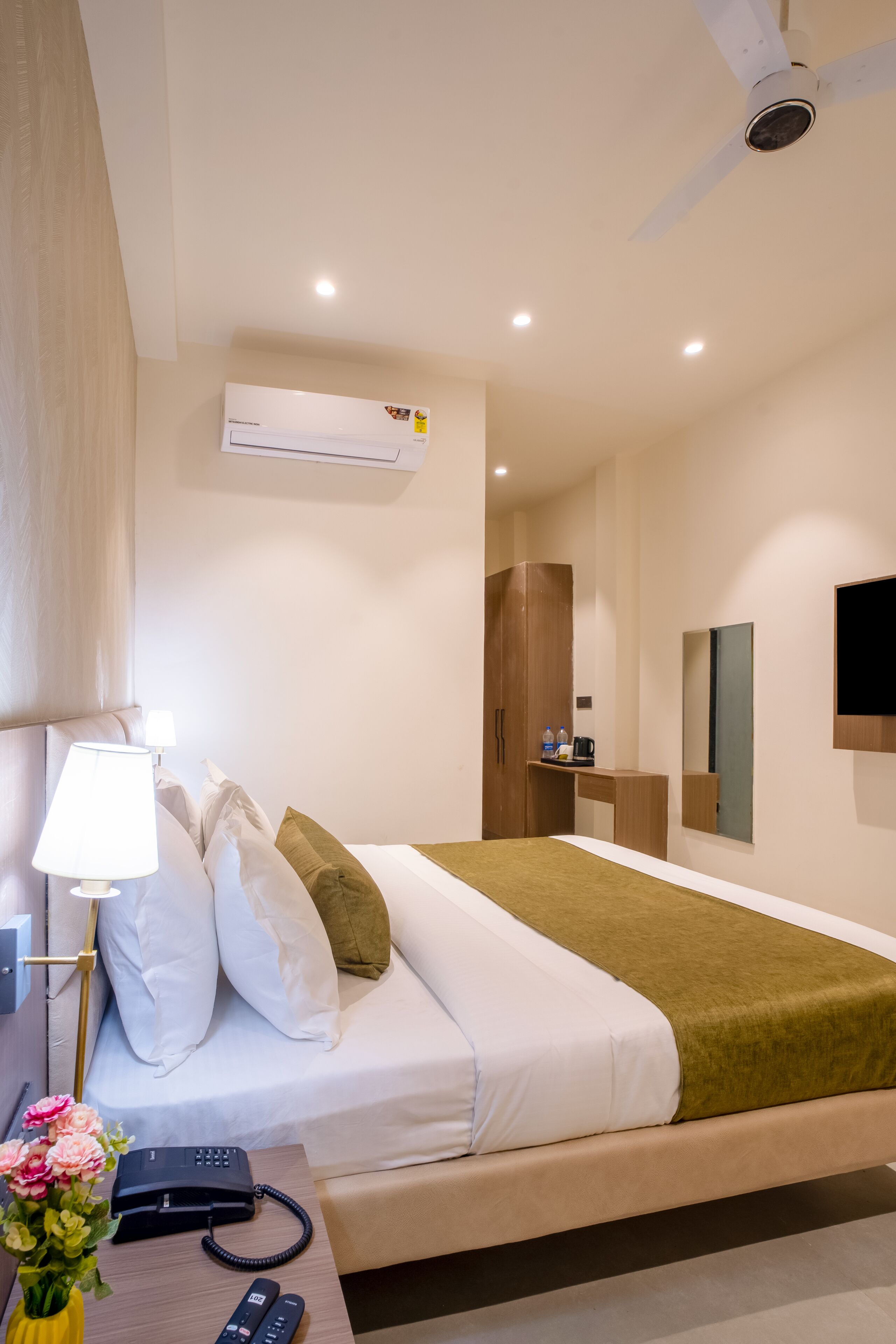 Una habitación de hotel moderna con cama, mesita de noche, lámpara, teléfono y televisor montado en la pared.