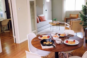 A dining area with a round wooden table set for breakfast, including pancakes and fruit. - Side-by-Side Homes - Near Zoo & Gaslamp (San Diego)