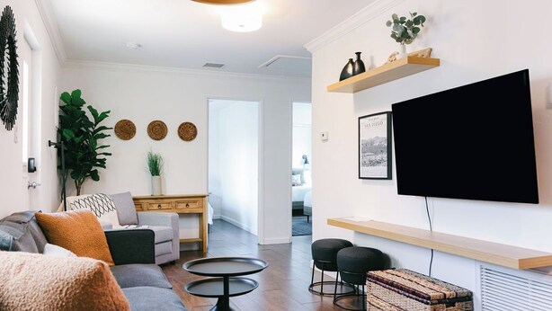 Ein modernes Wohnzimmer mit einer Couch, einem Couchtisch und einem an der Wand befestigten Fernseher über einem Holzboden.