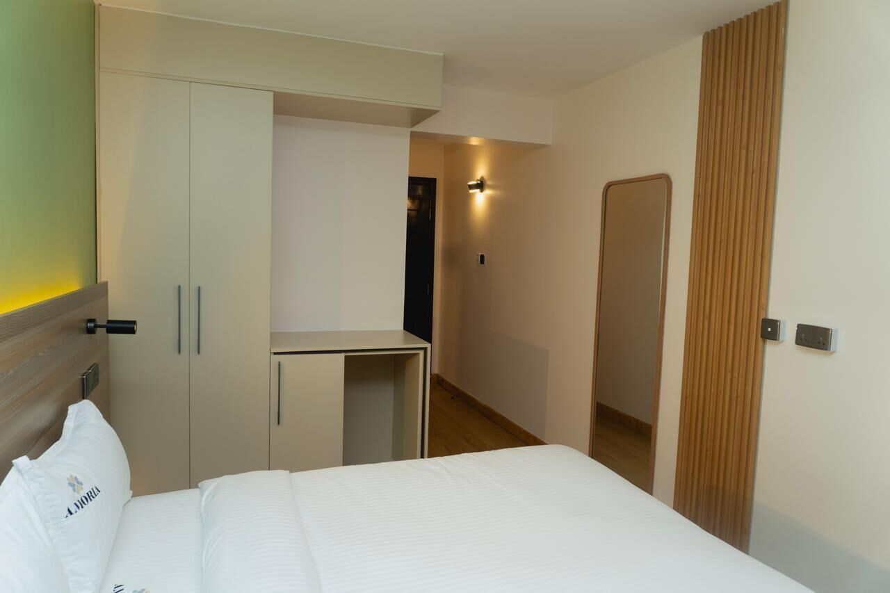 A hotel room with a bed, a wardrobe, a desk, and a mirror.