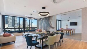 A modern living room with a dining area, large windows, and a city view. - Skyline Views & Pool | 2 King Beds, 2 Baths | Walk to South Bank | Free Parking (South Brisbane)