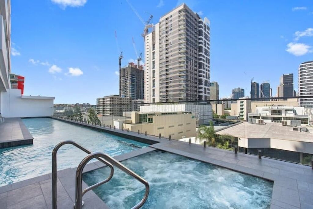 A rooftop swimming pool with a view of high-rise buildings and construction cranes in the background.