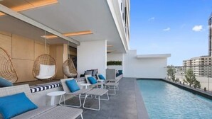 A rooftop pool area with lounge chairs, a hanging chair, and a small table. - Skyline Views & Pool | 2 King Beds, 2 Baths | Walk to South Bank | Free Parking (South Brisbane)