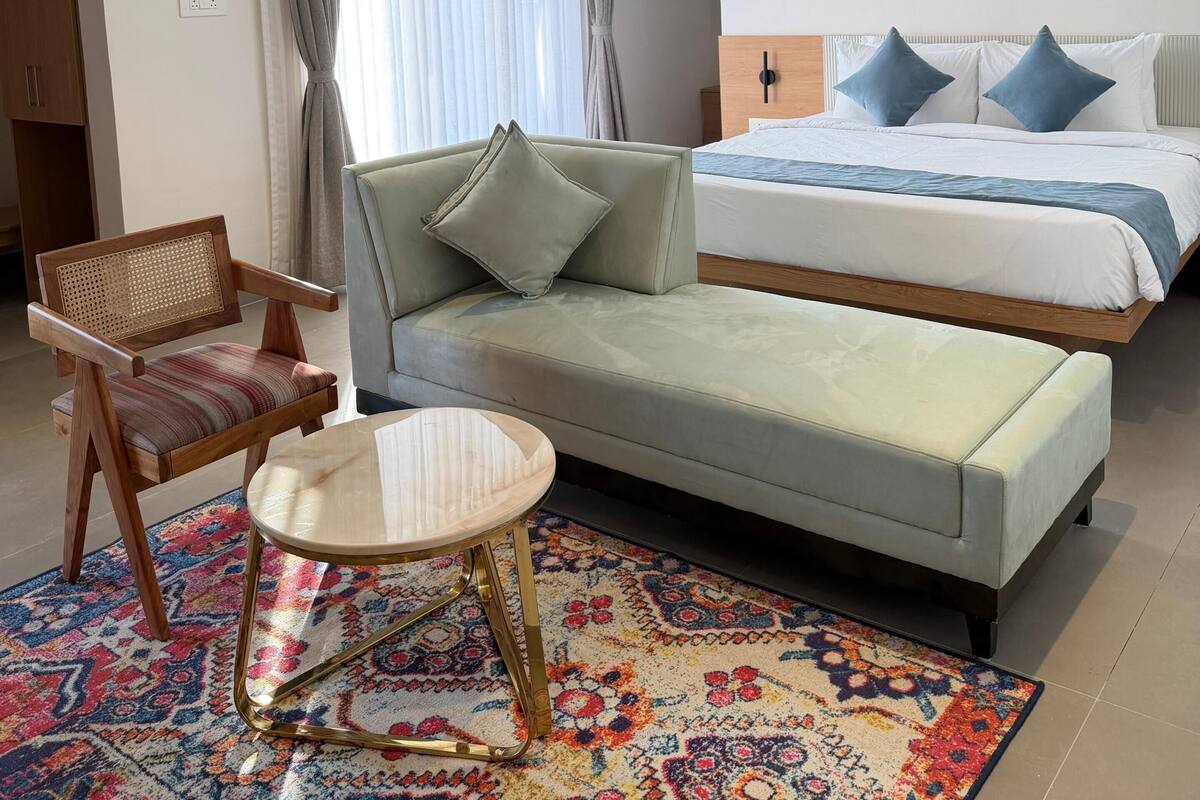 Et moderne hotelværelse med seng, sofa, stol, lille bord og ventilator.