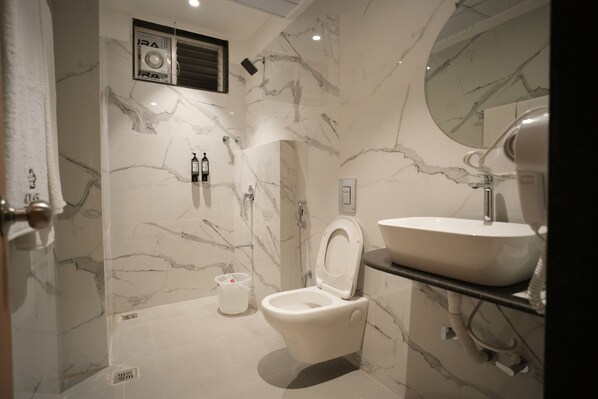 A modern bathroom with a marble wall, a toilet, a sink, and a mirror. - kolas grand (Warangal)