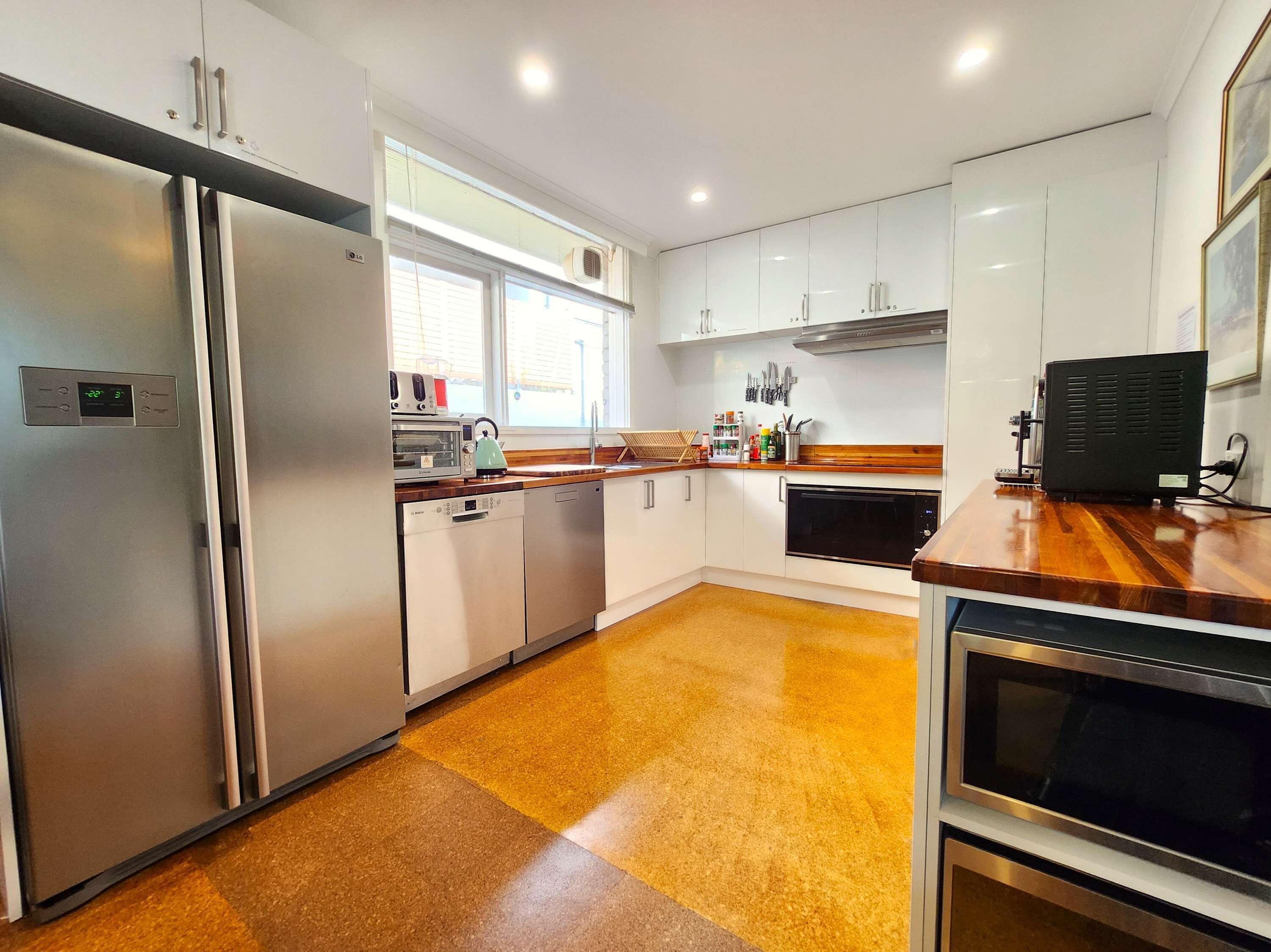 A modern kitchen with stainless steel appliances, white cabinetry, and a wooden countertop.