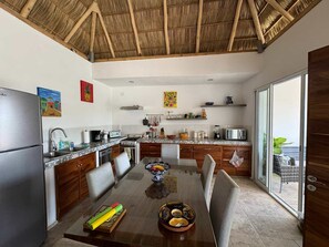 A modern kitchen with a dining area, featuring a large island, wooden cabinets, and a thatched roof ceiling. - Bright and Spacious, and just a short walk to Beach and Restaurants (Bucerías)