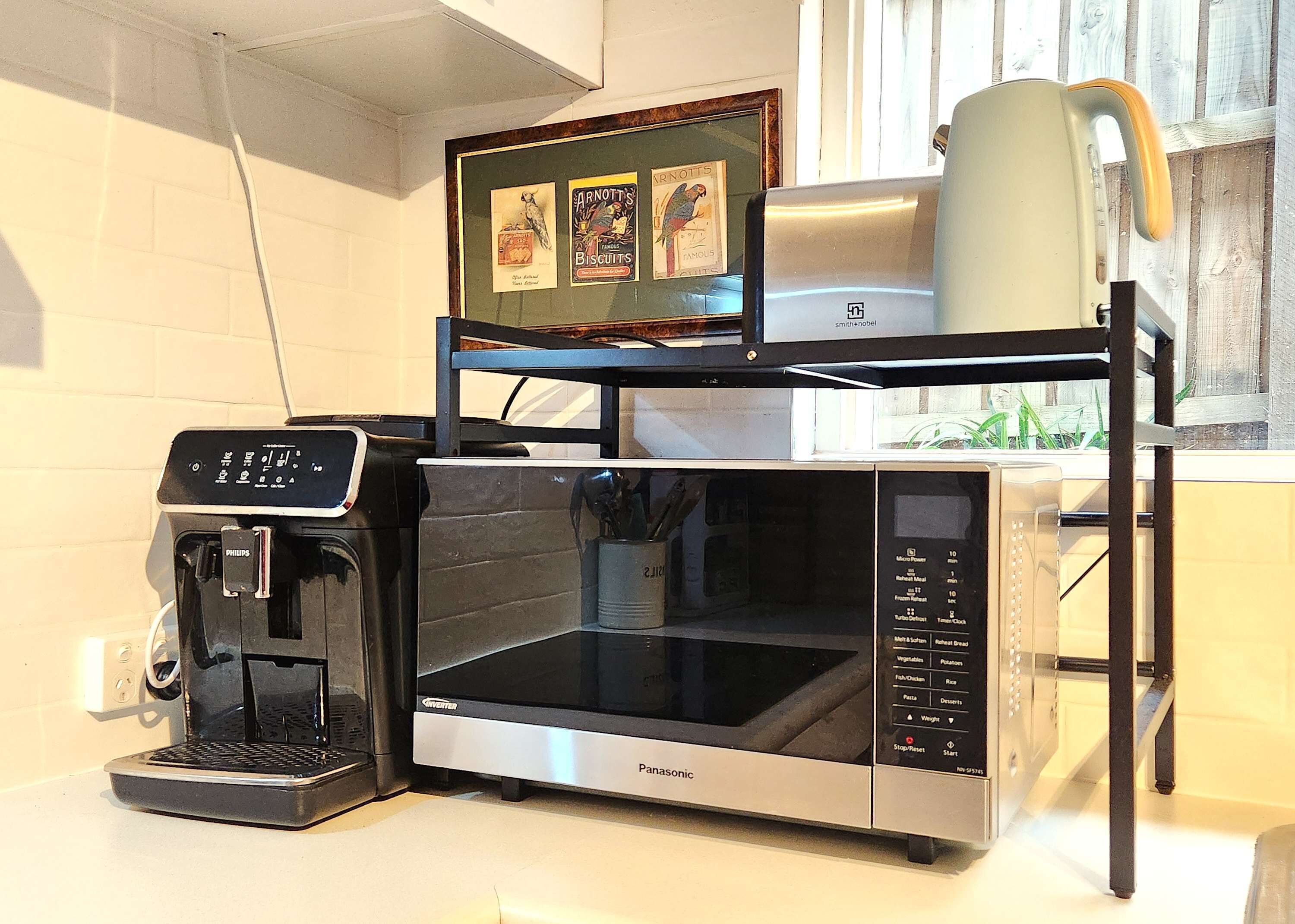 Una cucina con forno a microonde, macchina del caffè e bollitore su uno scaffale.