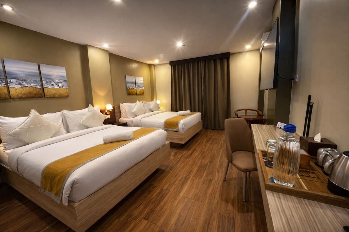 Ein Hotelzimmer mit zwei Betten, einem Schreibtisch, einem Sessel, einem Fernseher und Kunstwerken an den Wänden.