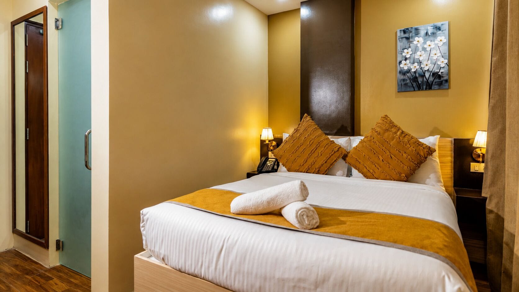 A hotel room with a bed, two bedside lamps, a painting on the wall, and a door.