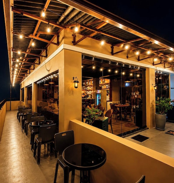 Un área de estar al aire libre con mesas y sillas, una sección techada con bar y vistas al interior.