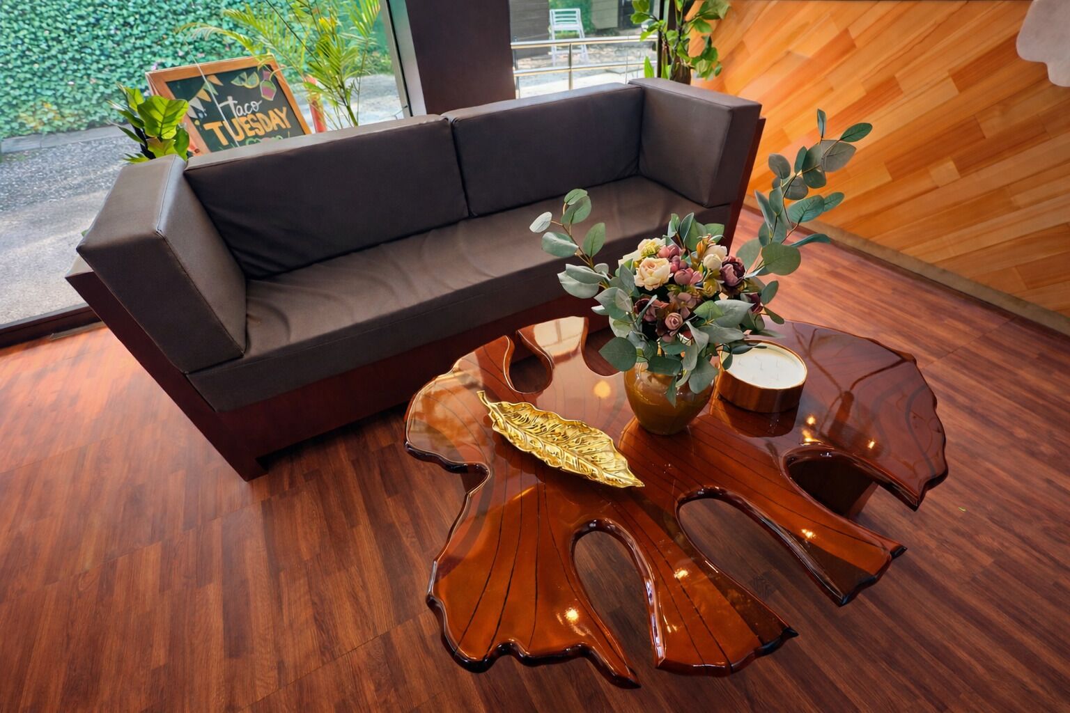 Ein modernes Interieur mit einem dunkelbraunen Sofa, einem einzigartigen Holztisch und einer Vase mit Blumen.