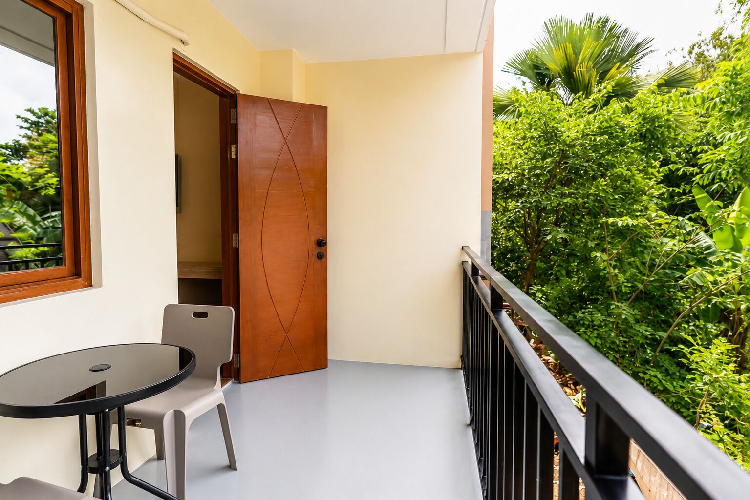 Un balcon avec une table et des chaises, une porte en bois et une vue sur une végétation luxuriante.