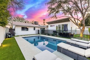 Ein modernes Haus mit Swimmingpool, einem umzäunten Garten und einer Terrasse mit Gartenmöbeln.