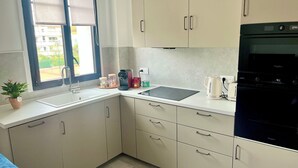 Uma cozinha moderna com armários brancos, fogão preto, cafeteira e janela com persianas.