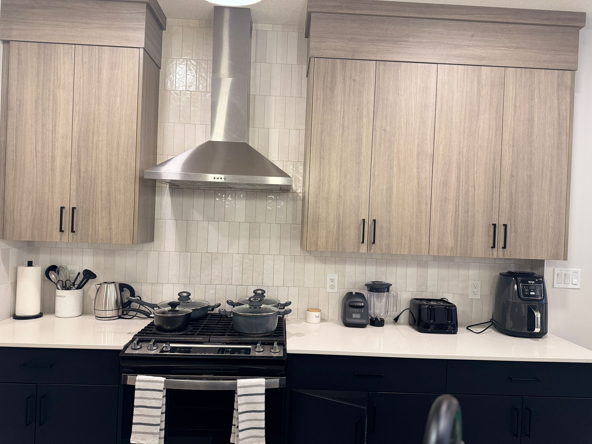 A modern kitchen with wooden cabinets, a stainless steel range hood, and a gas stove.