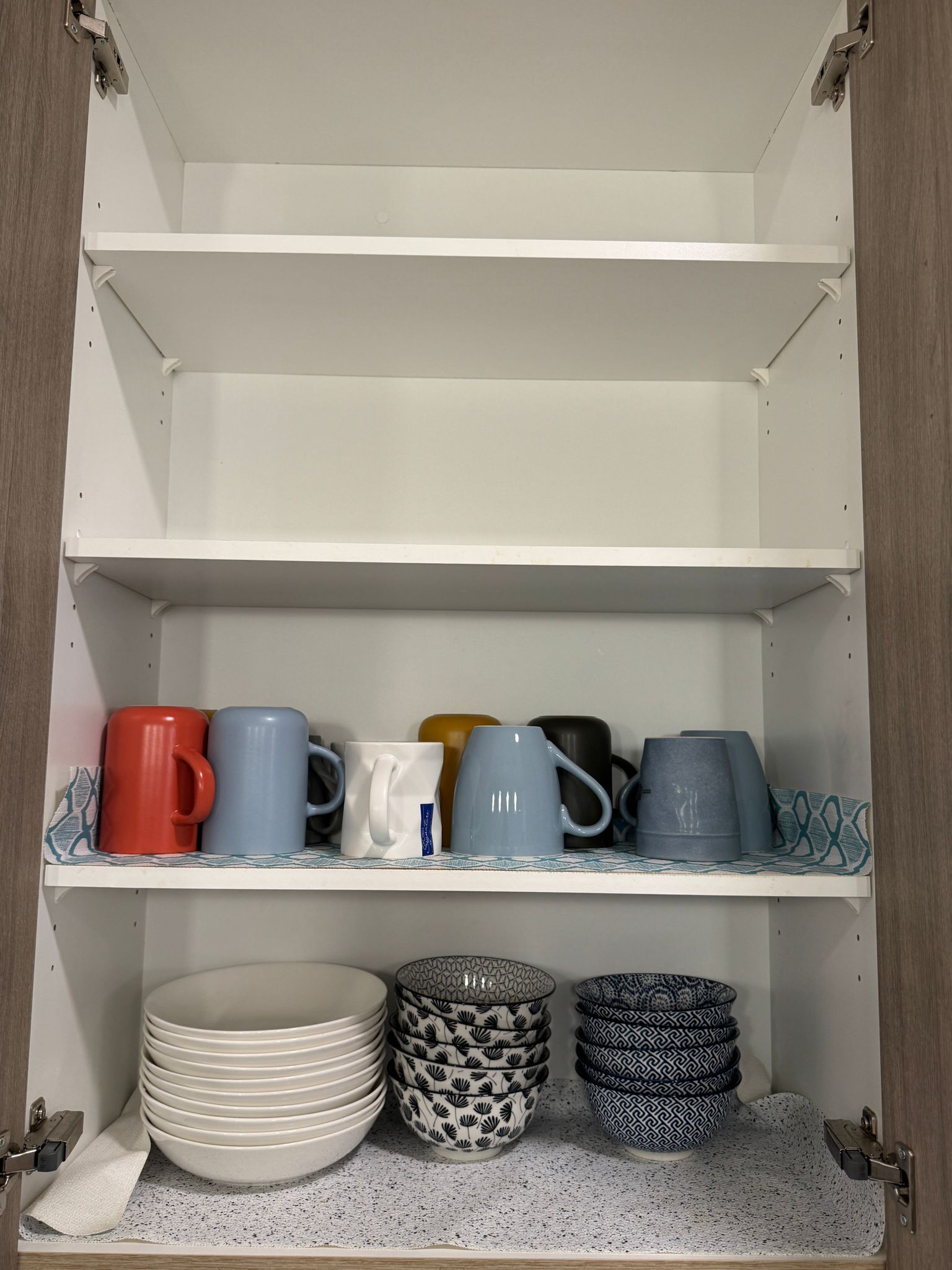 Un meuble avec des étagères où sont rangées des tasses, des assiettes et des bols.