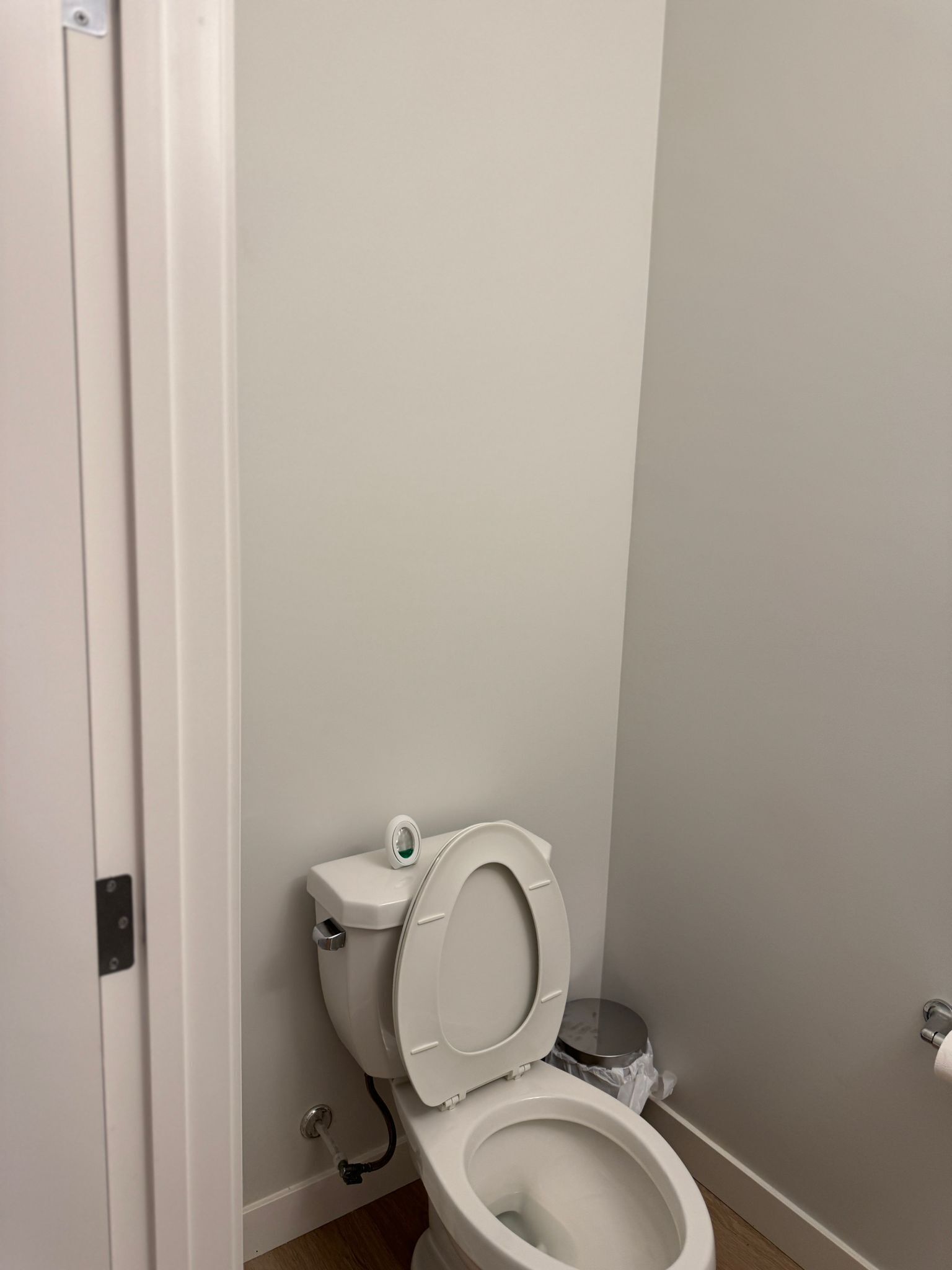A small, private bathroom with a white toilet, a small trash bin, and a door.