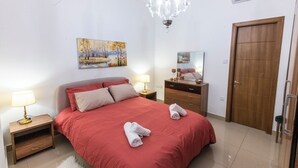 A bedroom with a bed, bedside tables, a chandelier, a door, and a painting on the wall. - Cosy APT in Sliema- 2 mins walk from sea (Sliema)