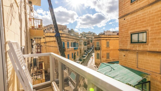 A balcony with a view of a narrow street lined with buildings, a crane, and a clear sky. - Cosy APT in Sliema- 2 mins walk from sea (Sliema)