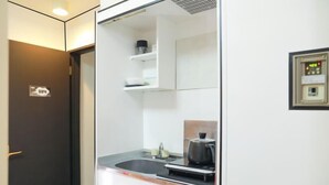 A modern kitchen with a built-in stove, sink, and a small countertop. - Oyasumi manga hotel (Osaka)
