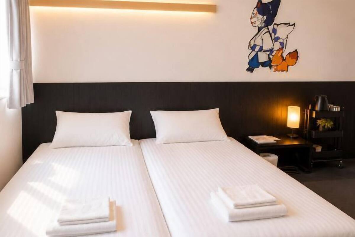 A hotel room with two beds, a nightstand with a lamp, and a wall decoration.