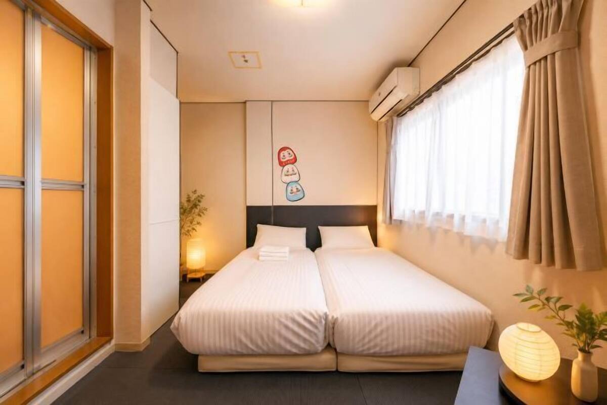 A double bed with a headboard, a bedside table with a lamp, and a window with curtains.