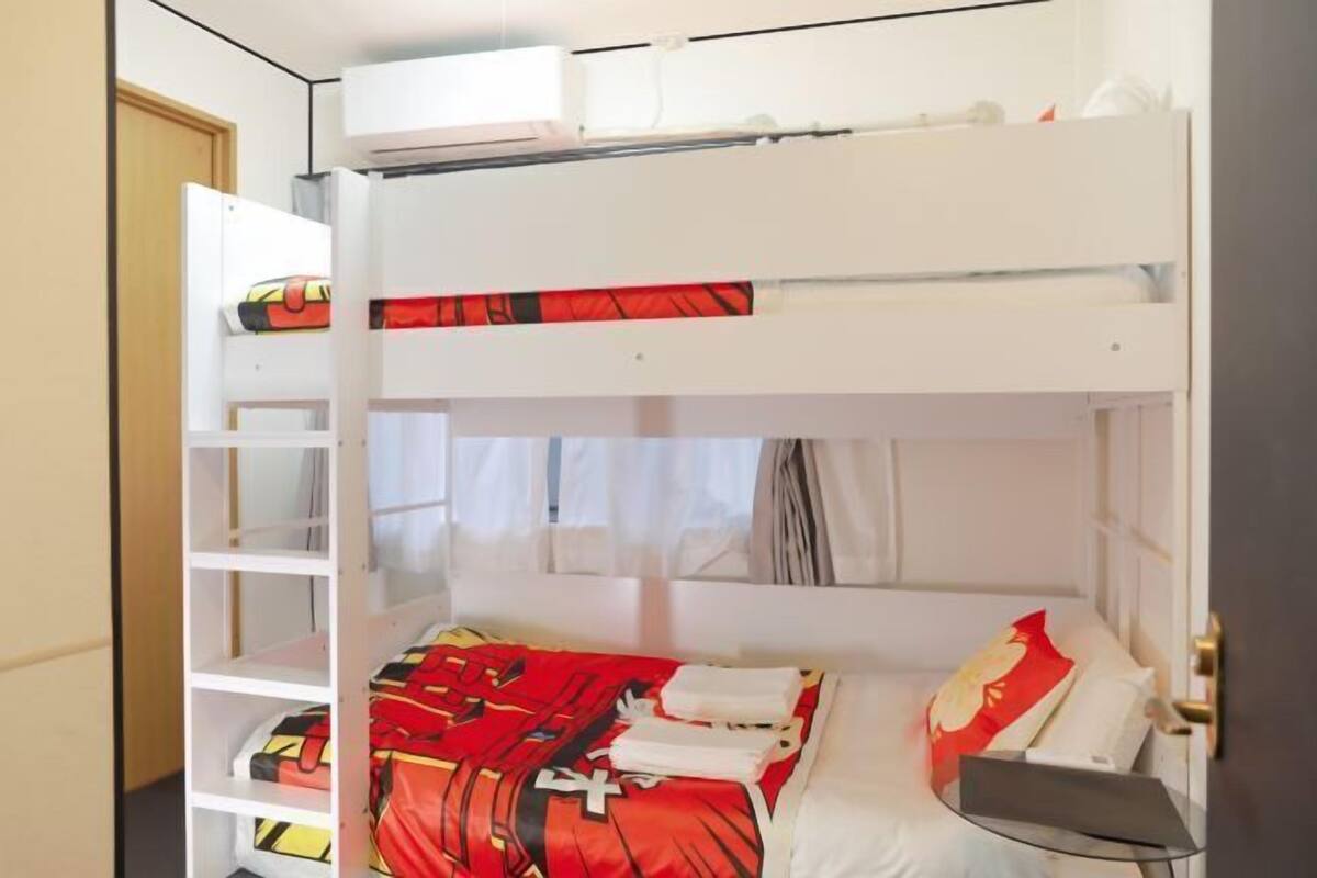 A bunk bed room with a white headboard, a small bedside table, and a window with curtains.