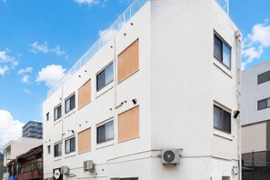 A multi-story building with a white facade, multiple windows, and a visible air conditioning unit. - Oyasumi manga hotel (Osaka)