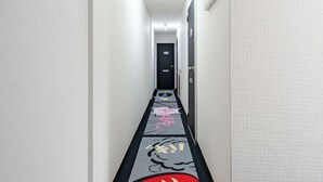 A narrow hallway with a patterned carpet, a door at the end, and a light fixture on the ceiling. - Oyasumi manga hotel (Osaka)