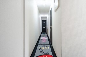 A narrow hallway with a patterned carpet, a door at the end, and a light fixture on the ceiling. - Oyasumi manga hotel (Osaka)