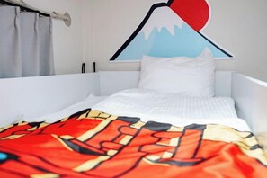 A bed with a white mattress and a colorful blanket, a pillow, and a wall decoration. - Oyasumi manga hotel (Osaka)