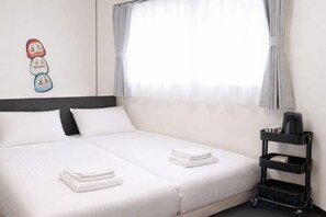 A hotel room with a bed, pillows, a bedside table, and a window with curtains. - Oyasumi manga hotel (Osaka)