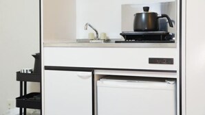 A compact kitchenette with a stove, sink, and a small refrigerator. - Oyasumi manga hotel (Osaka)